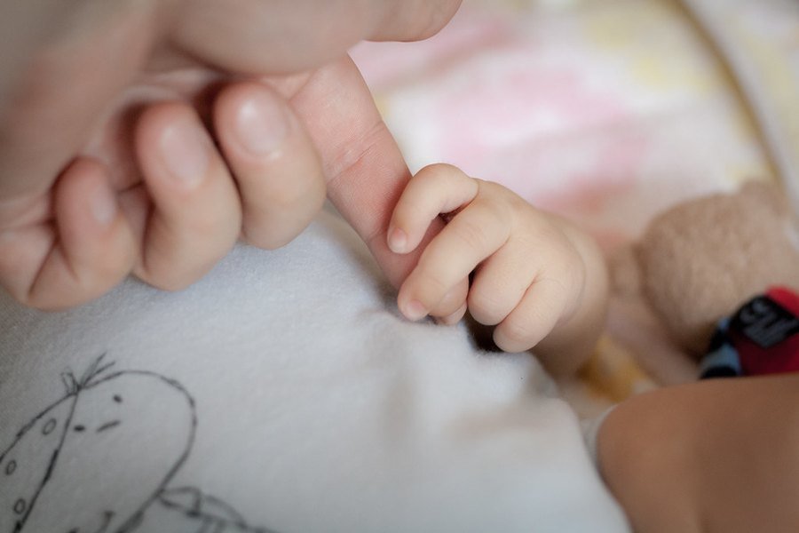 Mão de bebê segurando o dedo de um adulto